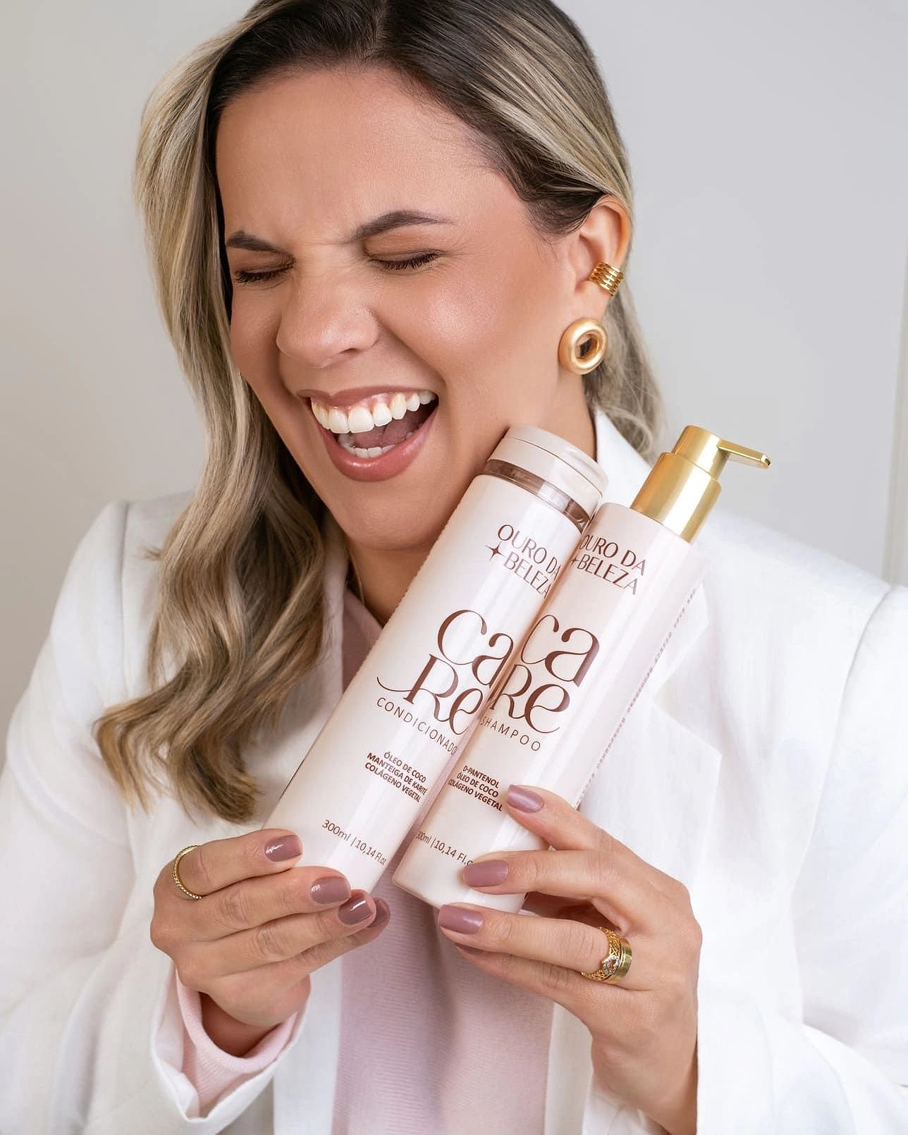 Idealizadora da Ouro da Beleza rindo, abraçando o Shampoo e o Condicionador CARE